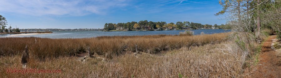 Dry marsh grasses line a broad stretch of blue water under scattered clouds.