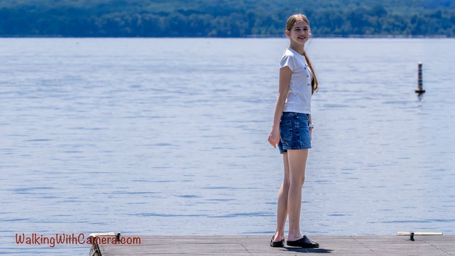 A person stands on a dock beside a broad expanse of water.