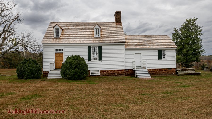 A white house with dormer windows and a brick chimney stands beneath gray clouds.