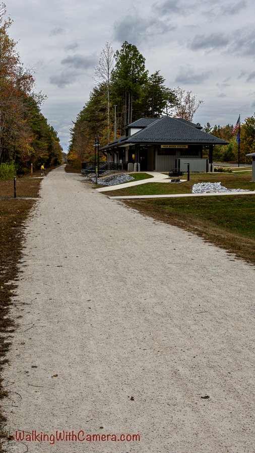 A pale gravel path leads toward a small dark-roofed building and autumn trees.