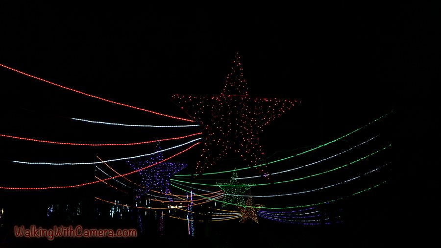 Thin red, white, and green light strands sweep across a dark scene. Fainter star-shaped decorations hang beyond the glowing lines.