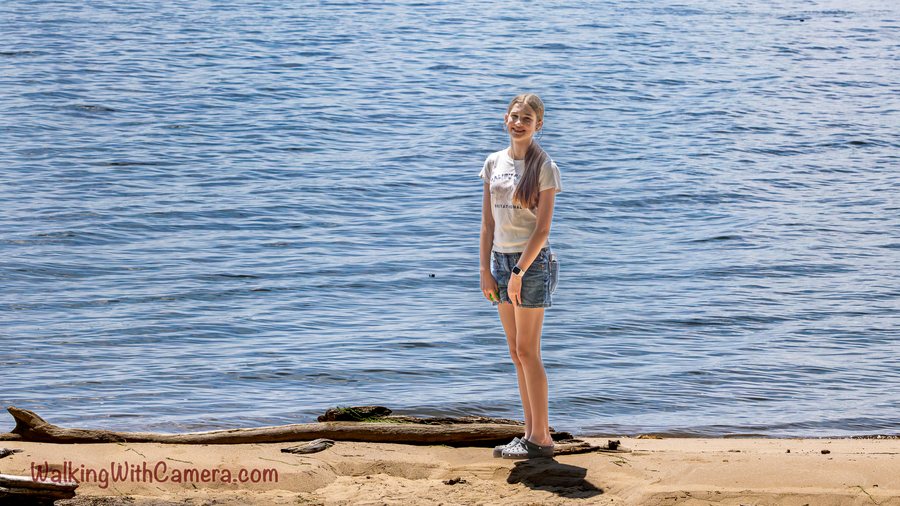 A person stands beside the water on a sandy shore.
