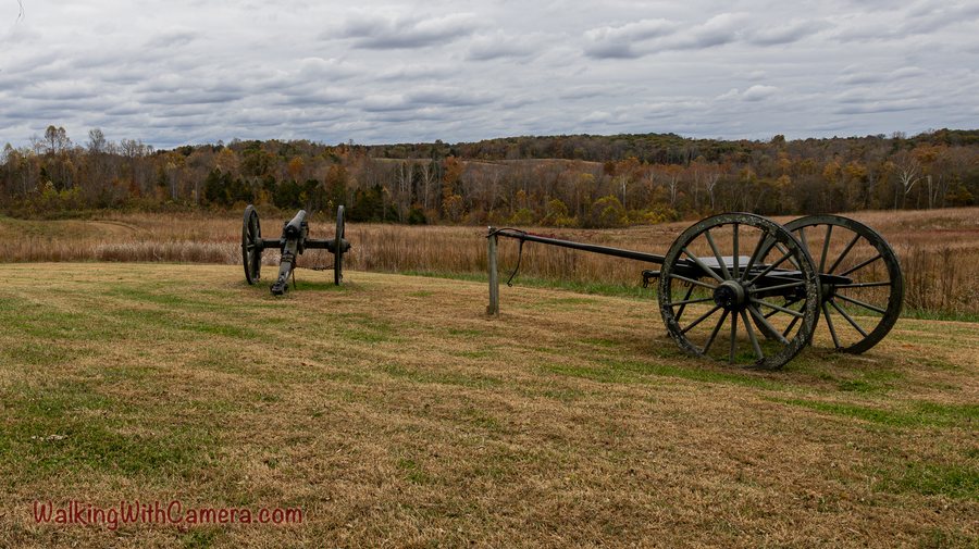 Two historic cannons stand in an open field beneath a cloudy sky.