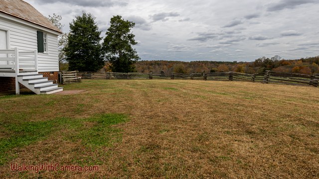The side of a white house overlooks a grassy slope and distant trees.