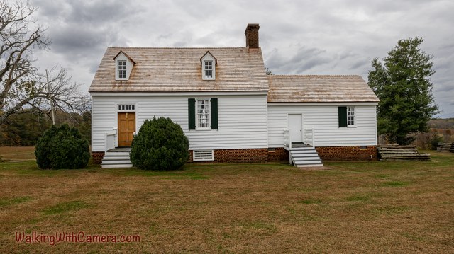 A white house with dormer windows and a brick chimney stands beneath gray clouds.