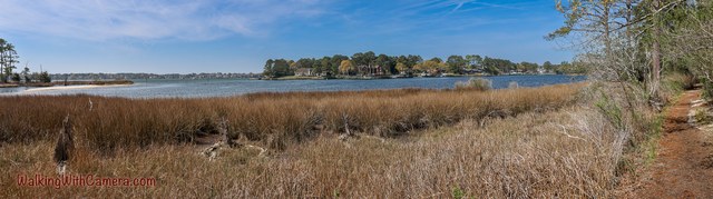 Dry marsh grasses line a broad stretch of blue water under scattered clouds.