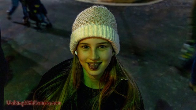 A person wearing a knitted hat smiles under colored evening lights.