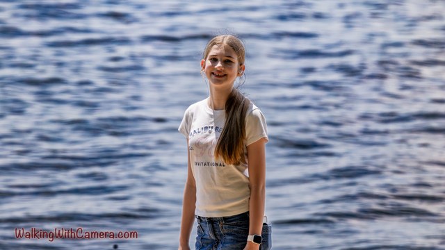 A person stands beside water with a relaxed smile. Ripples fill the blue background, and a light-colored shirt contrasts with the darker water.