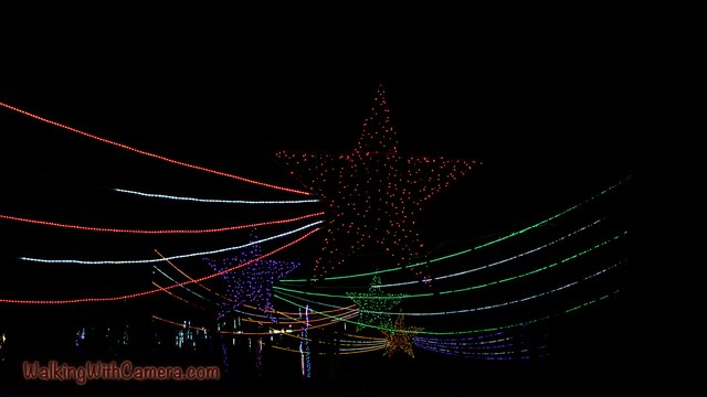 Thin red, white, and green light strands sweep across a dark scene. Fainter star-shaped decorations hang beyond the glowing lines.